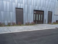 a black fire hydrant stands outside a building with metal cladding and plants in front