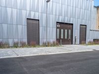 a black fire hydrant stands outside a building with metal cladding and plants in front