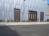 a black fire hydrant stands outside a building with metal cladding and plants in front