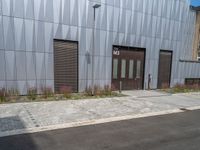 a black fire hydrant stands outside a building with metal cladding and plants in front