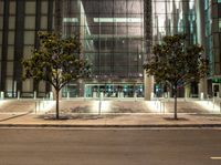 there are trees in front of the building at night, and some buildings in the background