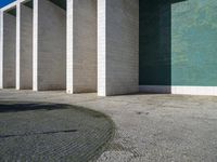 a wall and walkway near an open concrete area with a green wall on one side and blue tiles on the other side