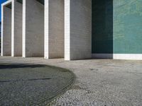 a wall and walkway near an open concrete area with a green wall on one side and blue tiles on the other side