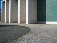 a wall and walkway near an open concrete area with a green wall on one side and blue tiles on the other side