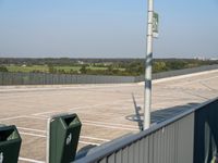 an empty parking lot with trash and trash containers in it on a sunny day by a fence