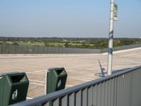 an empty parking lot with trash and trash containers in it on a sunny day by a fence