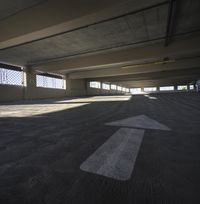 an empty parking garage with a white arrow on the ground and an angle perspective looking towards windows in the back