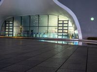 a building with large windows lit up at night in front of a pool outside of it