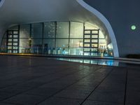 a building with large windows lit up at night in front of a pool outside of it