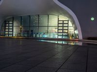 a building with large windows lit up at night in front of a pool outside of it