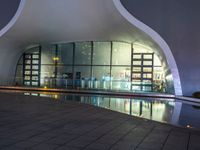 a building with large windows lit up at night in front of a pool outside of it