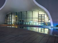 a building with large windows lit up at night in front of a pool outside of it