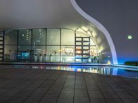 a building with large windows lit up at night in front of a pool outside of it