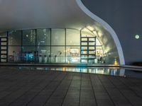 a building with large windows lit up at night in front of a pool outside of it