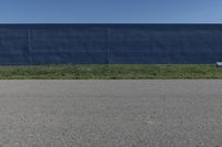 a blue wall is behind the empty road as a yellow fire hydrant stands near