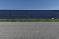 a blue wall is behind the empty road as a yellow fire hydrant stands near