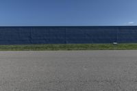 a blue wall is behind the empty road as a yellow fire hydrant stands near