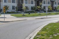 a yellow traffic sign sitting next to a green lawn and sidewalk next to a large apartment building