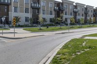 a yellow traffic sign sitting next to a green lawn and sidewalk next to a large apartment building