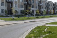 a yellow traffic sign sitting next to a green lawn and sidewalk next to a large apartment building