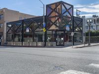 an empty street with a glass building on one corner and an intersection sign on the other side