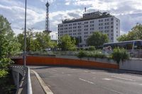 a long bus traveling down a highway near an apartment building in the city with the trees growing on the ground