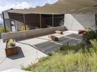 the outdoor area has two benches next to a concrete building with a large awning over it