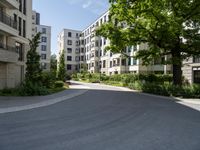 a street with parking meters and trees in front of a large building with apartments on each side