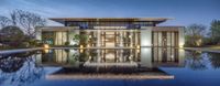 a glass walled house sitting in the middle of a pool at twilight with a lit reflection