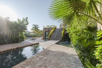 an outdoor pool that is surrounded by trees and landscaping shrubss near a building with stone walkway and palm leaves