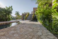 an outdoor pool that is surrounded by trees and landscaping shrubss near a building with stone walkway and palm leaves