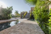 an outdoor pool that is surrounded by trees and landscaping shrubss near a building with stone walkway and palm leaves