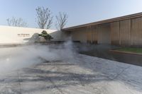 there is some steam in the courtyard of this building next to trees and grass near the wall