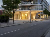 an office building at the corner of the road next to a sidewalk and some trees