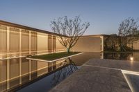 a reflecting pool in the middle of a building with lighted windows next to it and grass