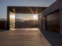 a sun shines over the mountains and entrance to an outdoor garage building, with wooden doors