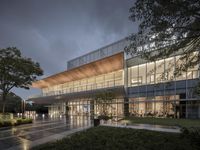 a building with glass windows and trees in front of it at night time with rain falling off