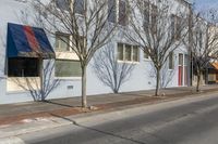 a row of trees next to a building and two shops along the road with a traffic light