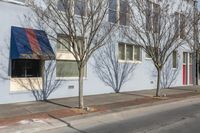 a row of trees next to a building and two shops along the road with a traffic light