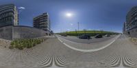 a panoramic picture of several cars parked in front of large buildings along a driveway