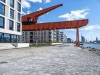 this red and orange crane is in a building complex with a river view in the background