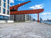 this red and orange crane is in a building complex with a river view in the background