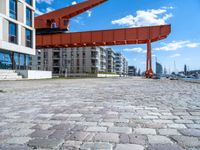 this red and orange crane is in a building complex with a river view in the background