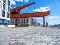 this red and orange crane is in a building complex with a river view in the background