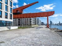 this red and orange crane is in a building complex with a river view in the background