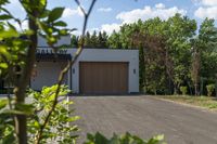 garage in a wooded area with a brown door and white exterior with red letters saying gallery