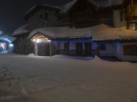 a picture of an outside home that is lit up for christmas night by snow on the ground