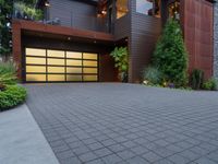 the driveway of this large home has black brick pavers in it, and lights are on