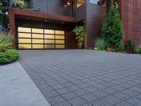 the driveway of this large home has black brick pavers in it, and lights are on