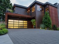 the driveway of this large home has black brick pavers in it, and lights are on